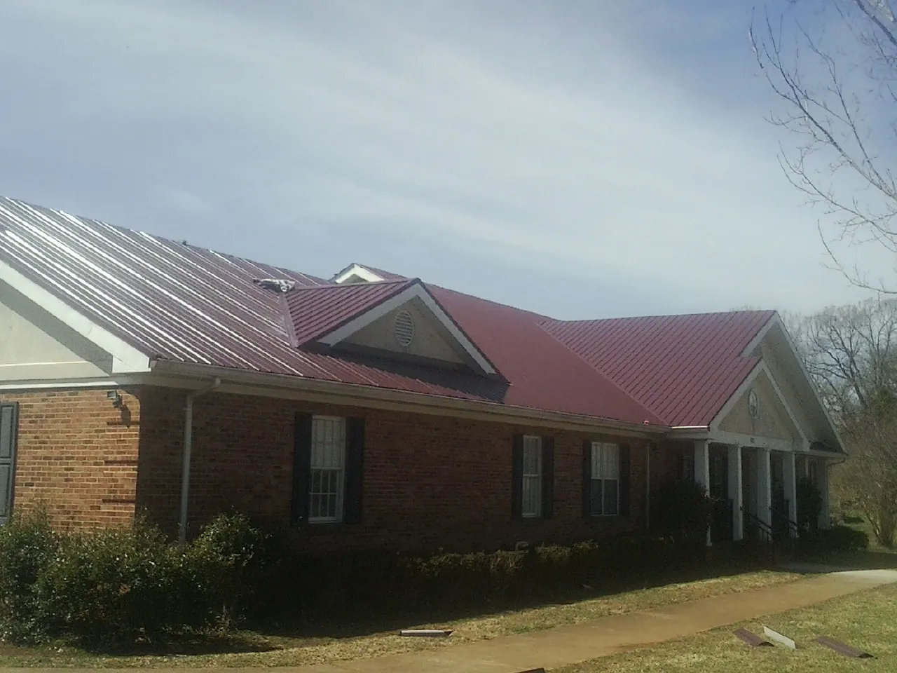 Red metal roof with gabled entries on a long brick building, from a Hail Damage Roof Repair job in Buhl