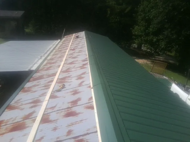 Old rusted panels beside newly installed green metal roofing — Wind Damage Roof Repair by Roofing Brothers in Buhl