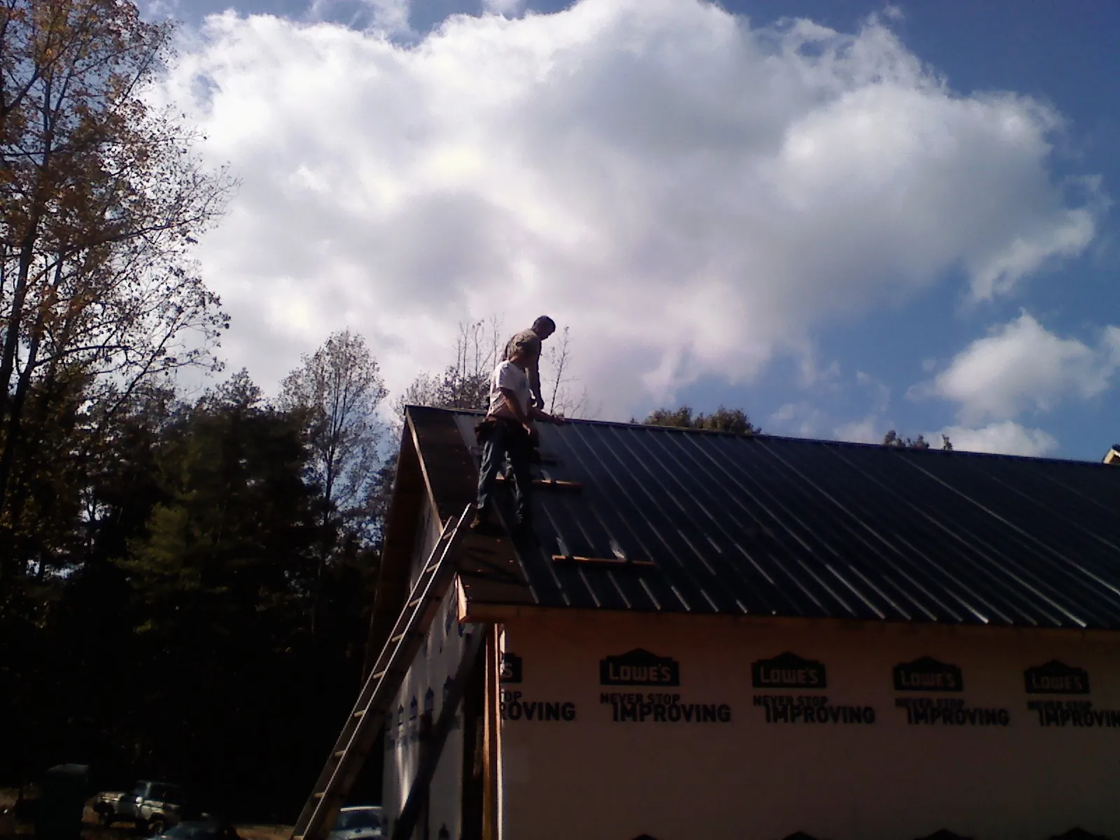 Roofer fastening dark metal panels high against a cloudy sky, from a Roof Inspection job in Buhl