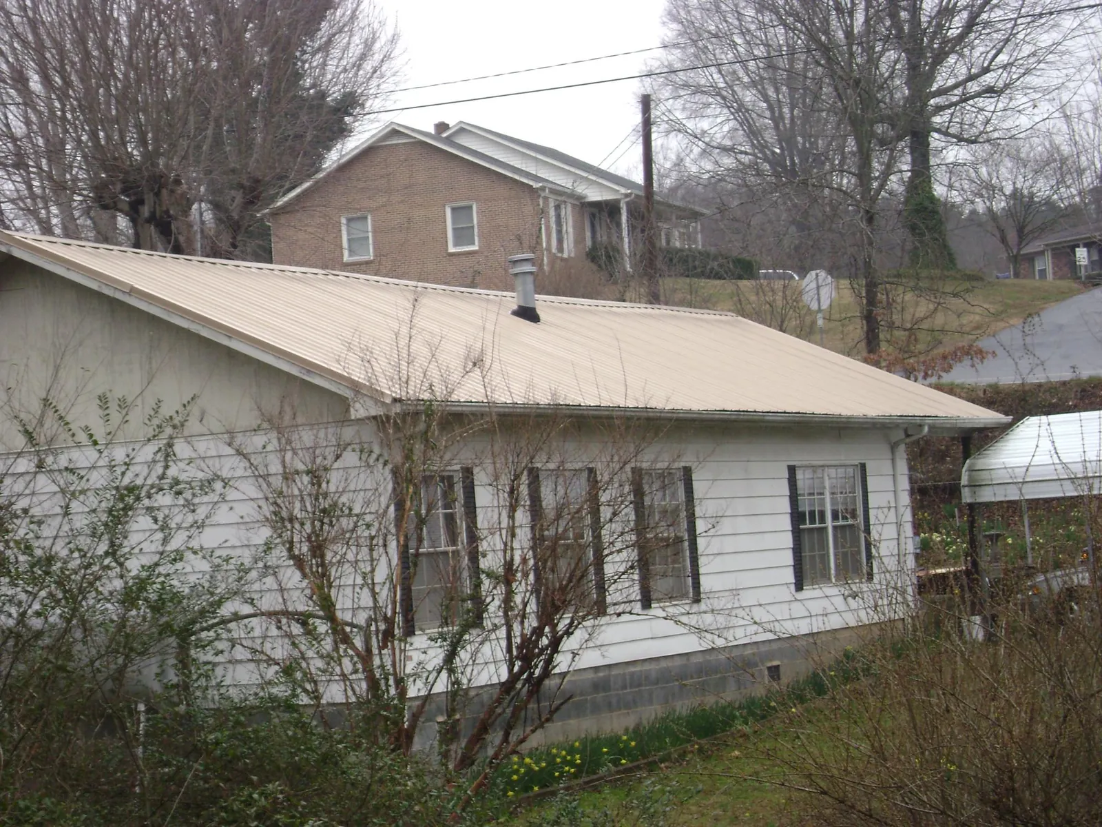 Tan metal roof on a white sided house set into a hillside — Commercial Roofing by Roofing Brothers in Buhl