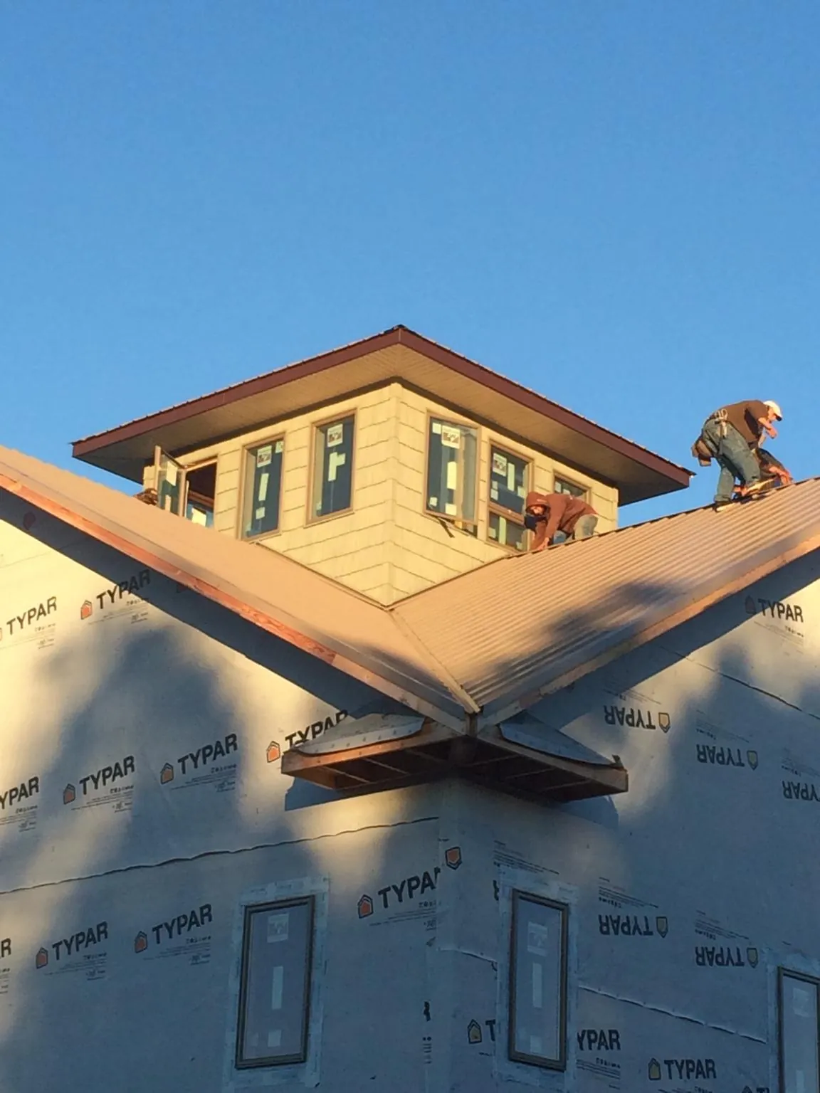 Roofers working around a rooftop cupola on a new metal roof at sunset in Buhl
